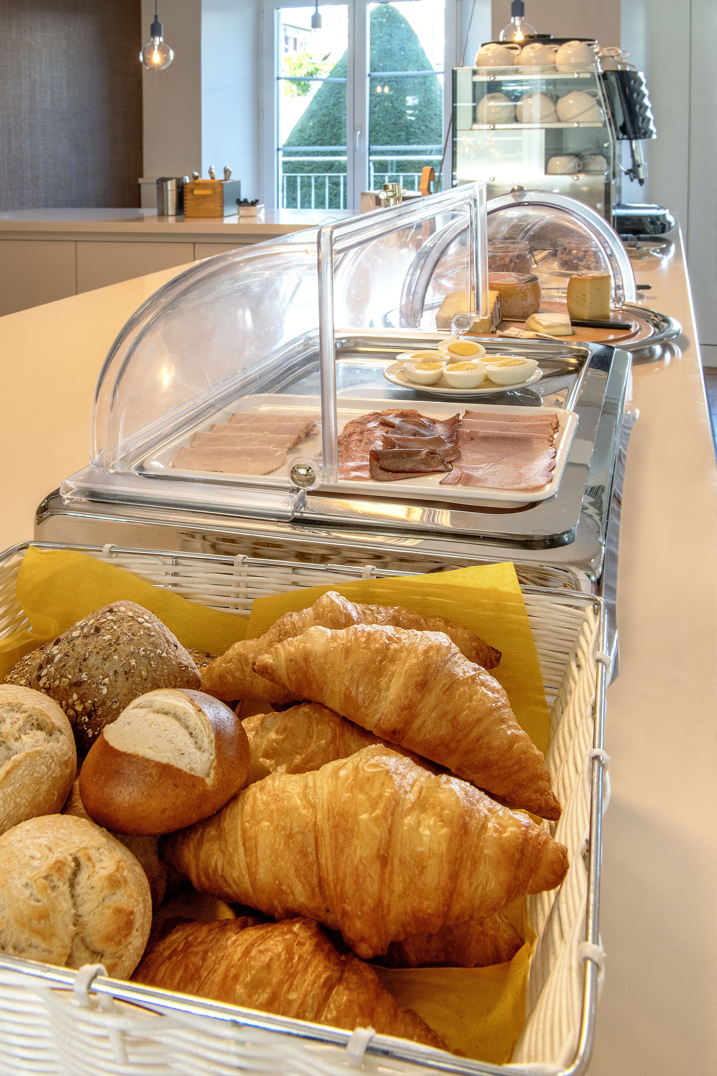 Um buffet com diversos pães e produtos de pastelaria, incluindo croissants e baguetes, expostos em cestas.