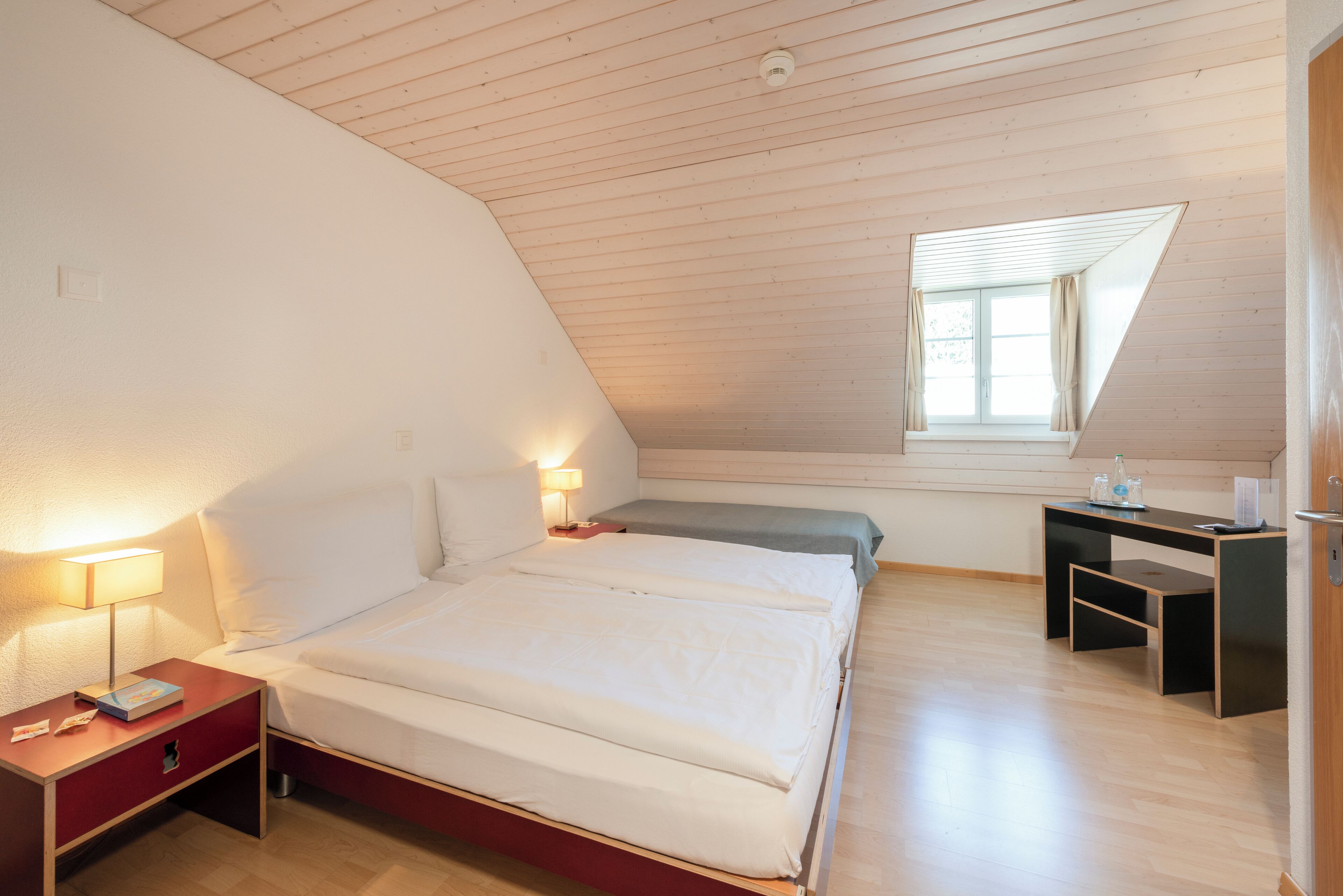 Een slaapkamer met een bed, nachtkastjes, een bureau en een raam.
