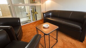 Une pièce avec un canapé en cuir noir, une petite table en bois et une porte en verre donnant sur un balcon.
