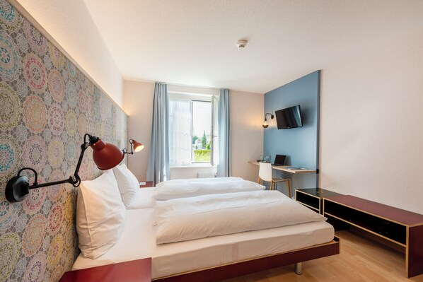 A modern bedroom with a bed, a desk, a TV, and a window with curtains.