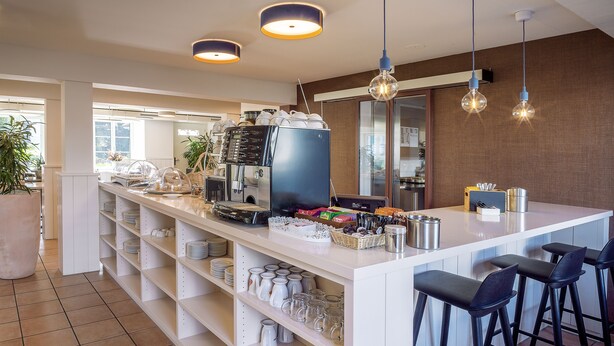 Une cuisine moderne équipée d’une machine à café, de tabourets de bar et d’étagères remplies d’ustensiles de cuisine.