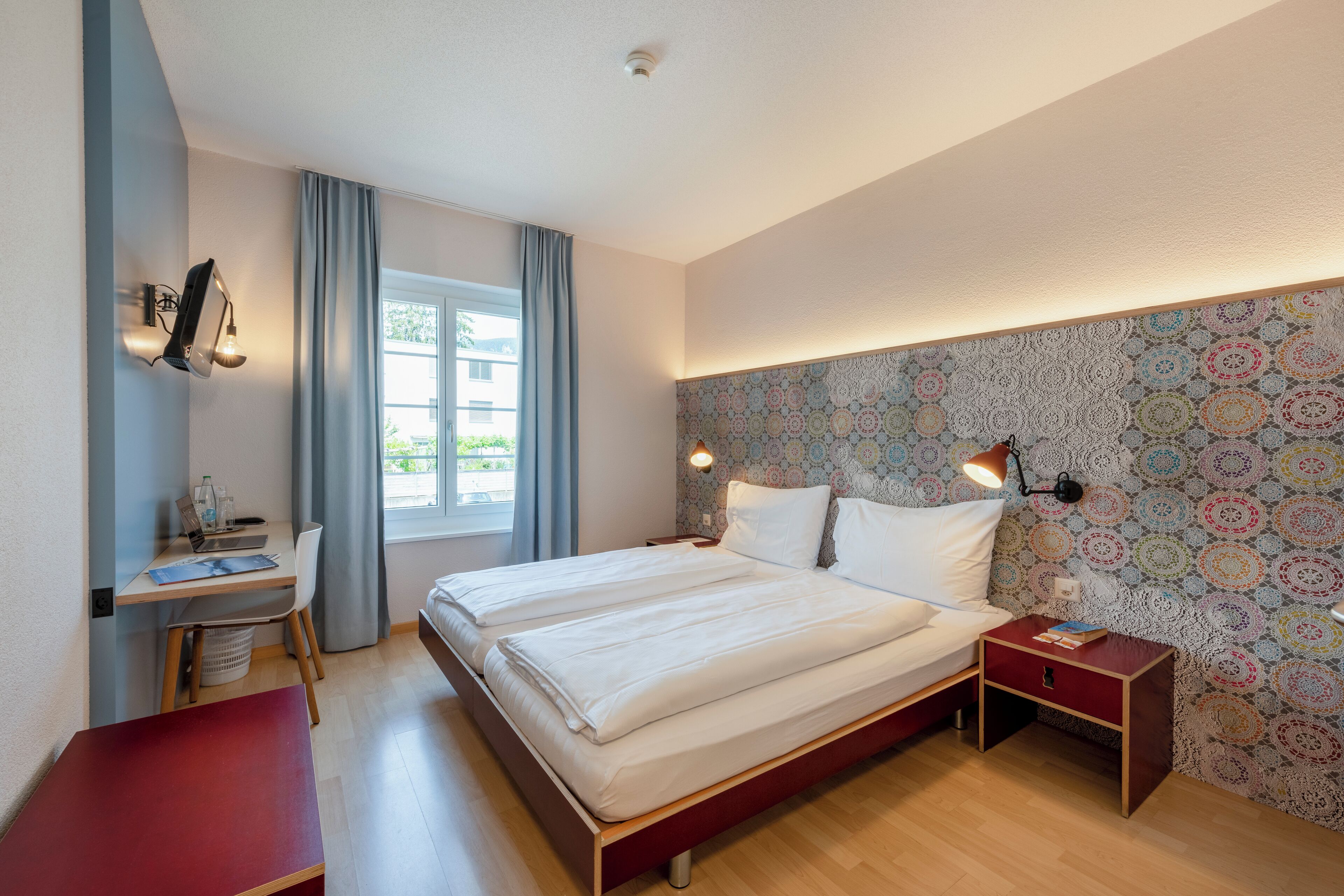 A bedroom with a bed, bedside tables, a desk, and a chair.