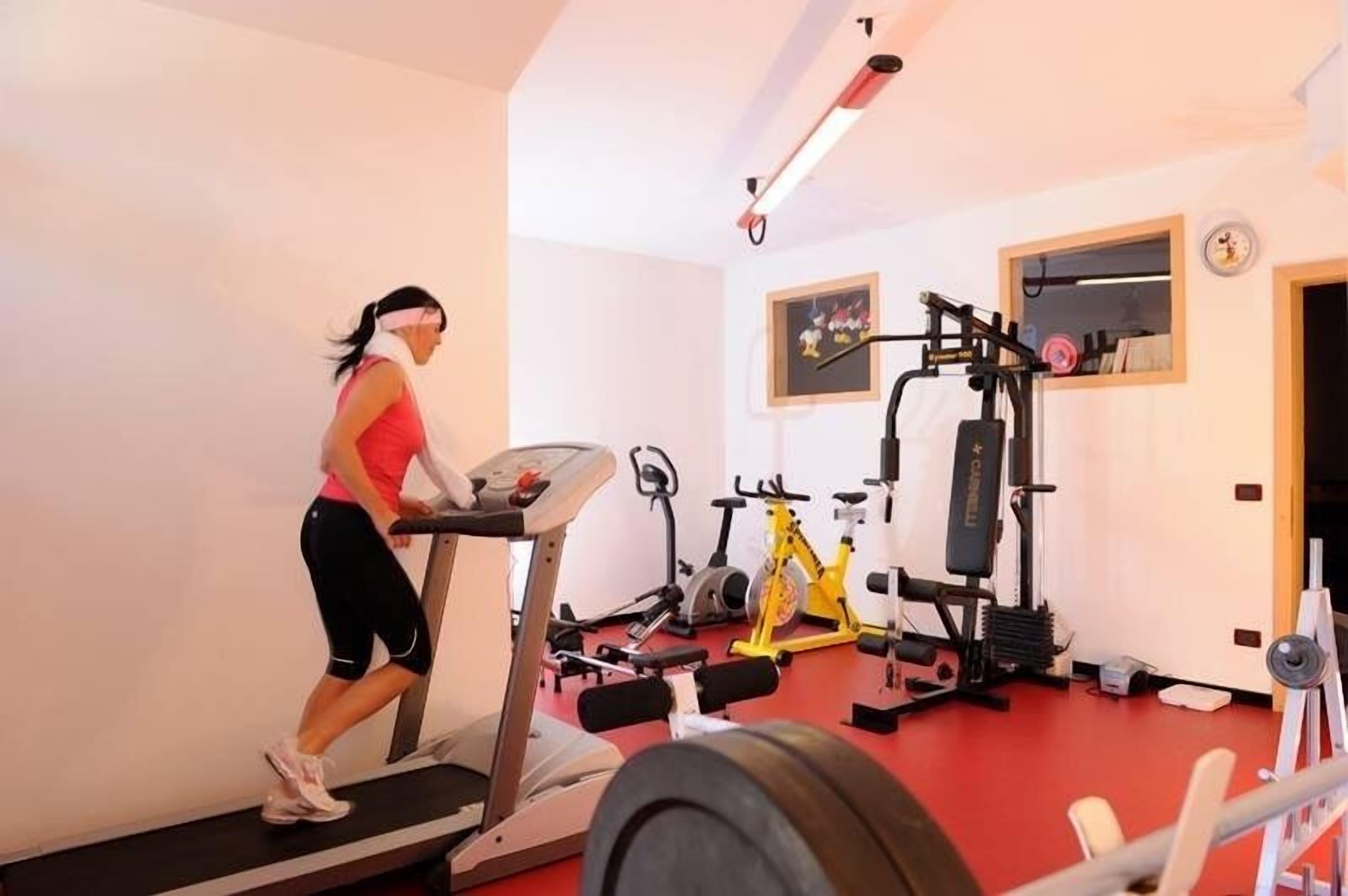 Eine Frau läuft auf einem Laufband in einem Fitnessstudio mit unterschiedlichen Trainingsgeräten.