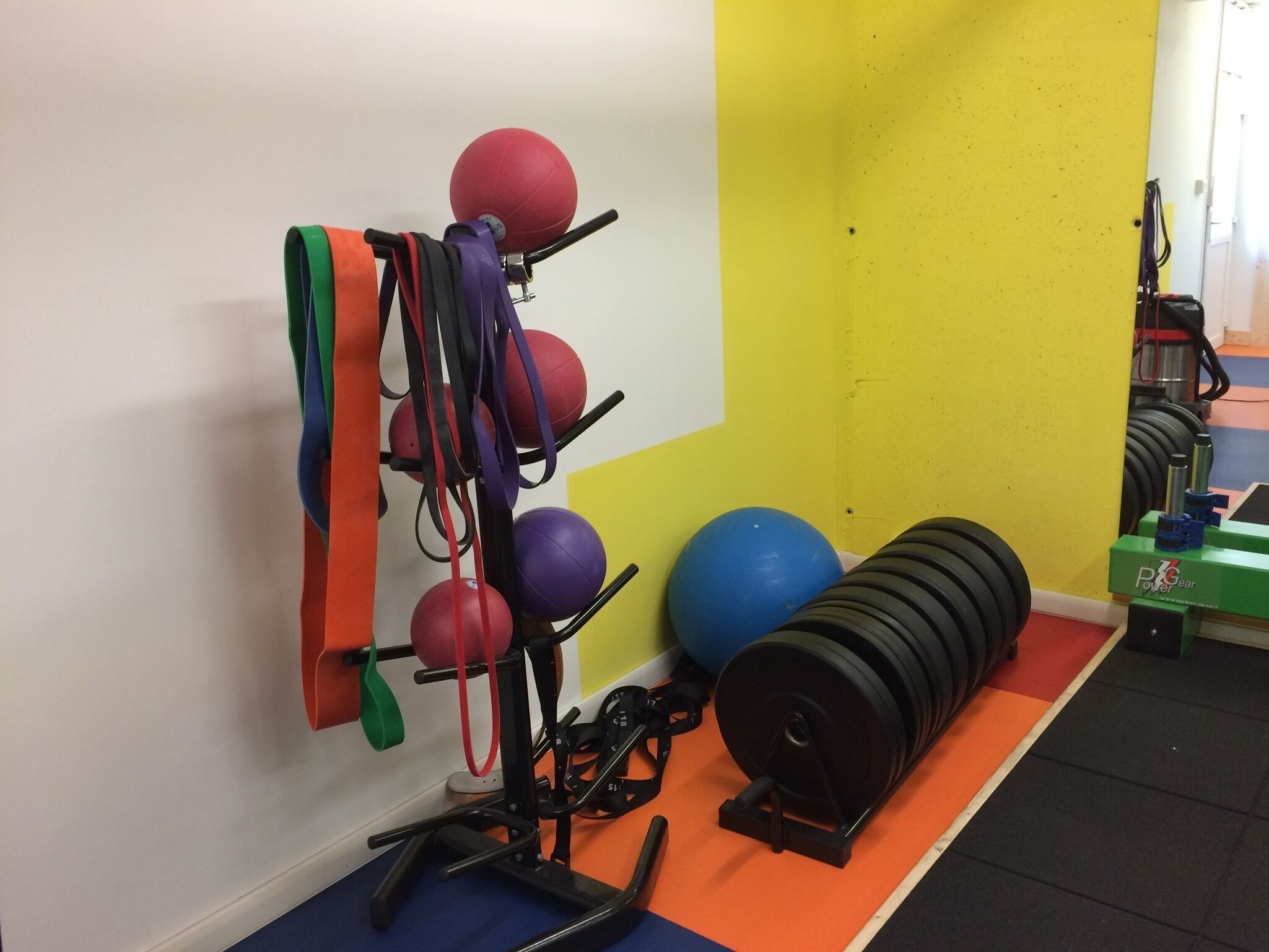 Un gimnasio con equipo de ejercicio, que incluye un soporte de pared para balones, un balón azul y una pila de discos de pesas.