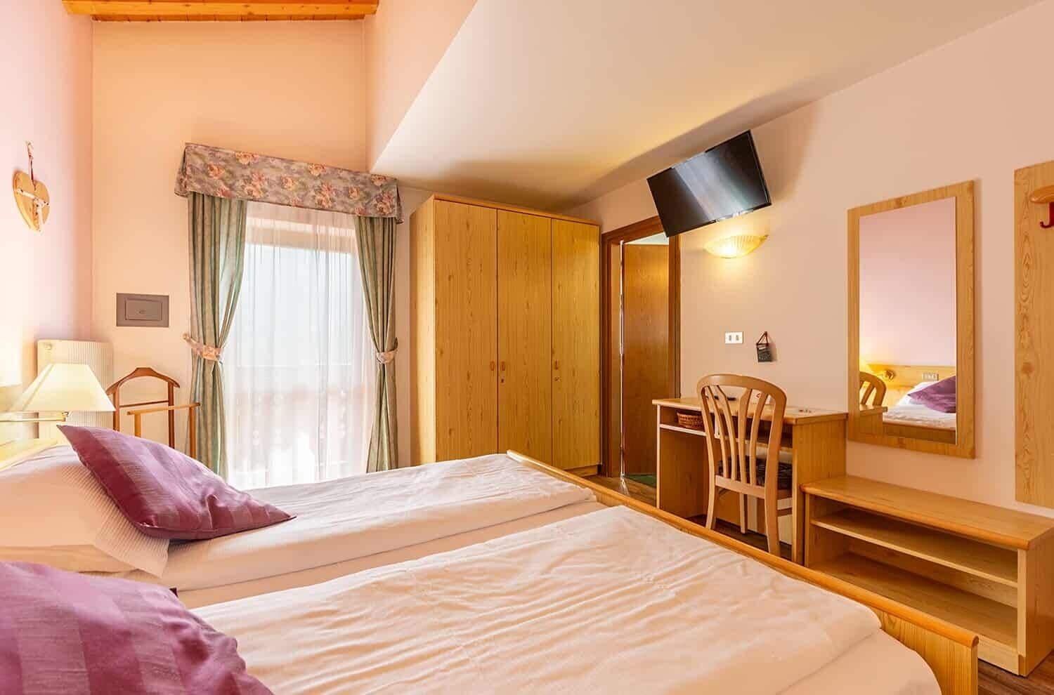 A hotel room with two beds, a desk, a chair, a TV, and a wardrobe.