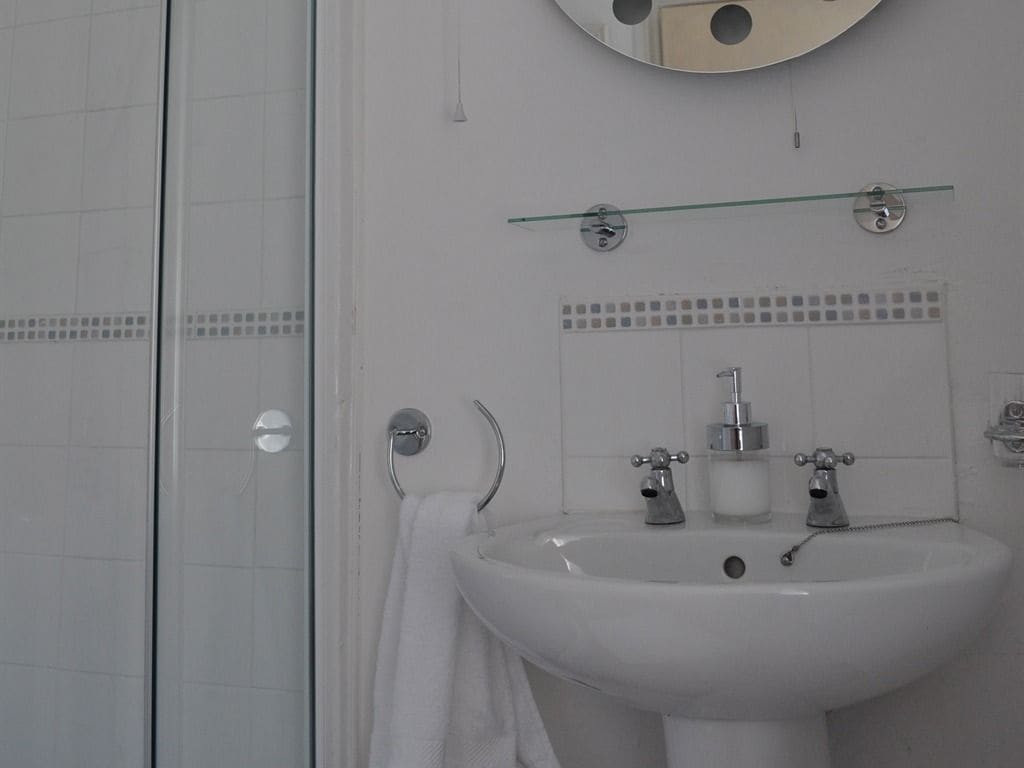 Une salle de bain avec un lavabo blanc, un miroir et une cabine de douche en verre.