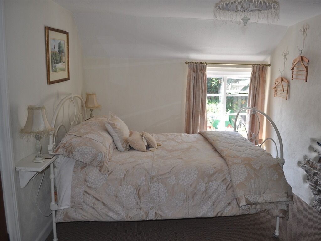 A bedroom with a bed, a bedside table with a lamp, a window with curtains, and wall-mounted birdcages.