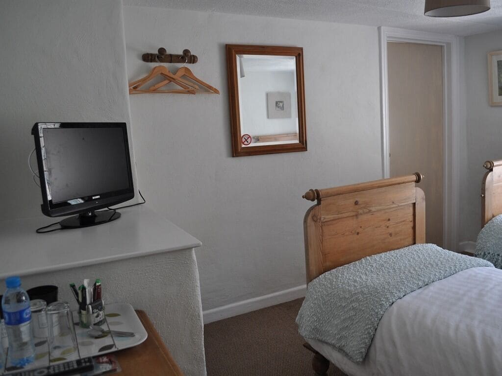 Een hotelkamer met een bed, een bureau met een computerscherm, een spiegel en een deur.