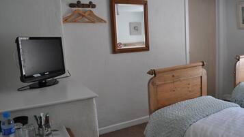 Een hotelkamer met een bed, een bureau met een computerscherm, een spiegel en een deur.