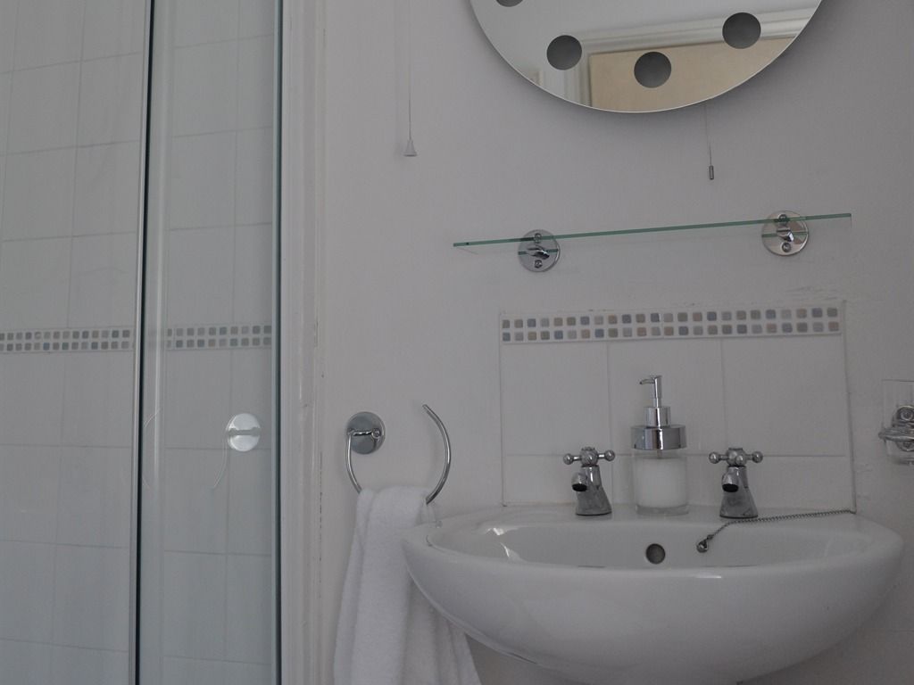 A bathroom with a white sink, a mirror, and a glass shelf above it.