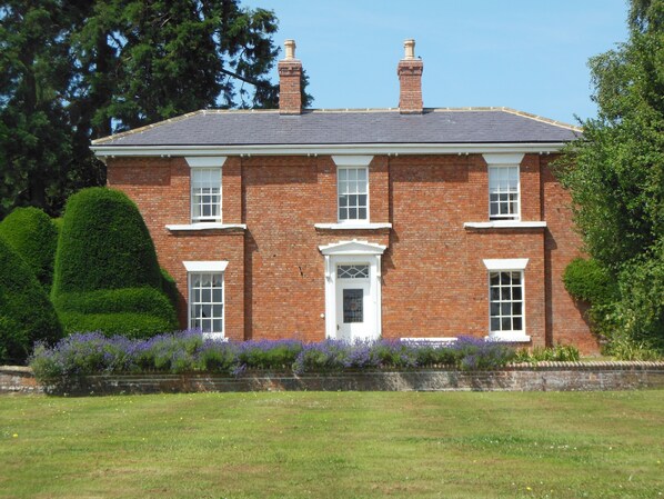 A two-story brick house with a symmetrical facade, a central entrance with a white door, and a small porch.