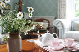 A room with a wooden table, a vase with white flowers, a teapot, and a tray with teacups and saucers.