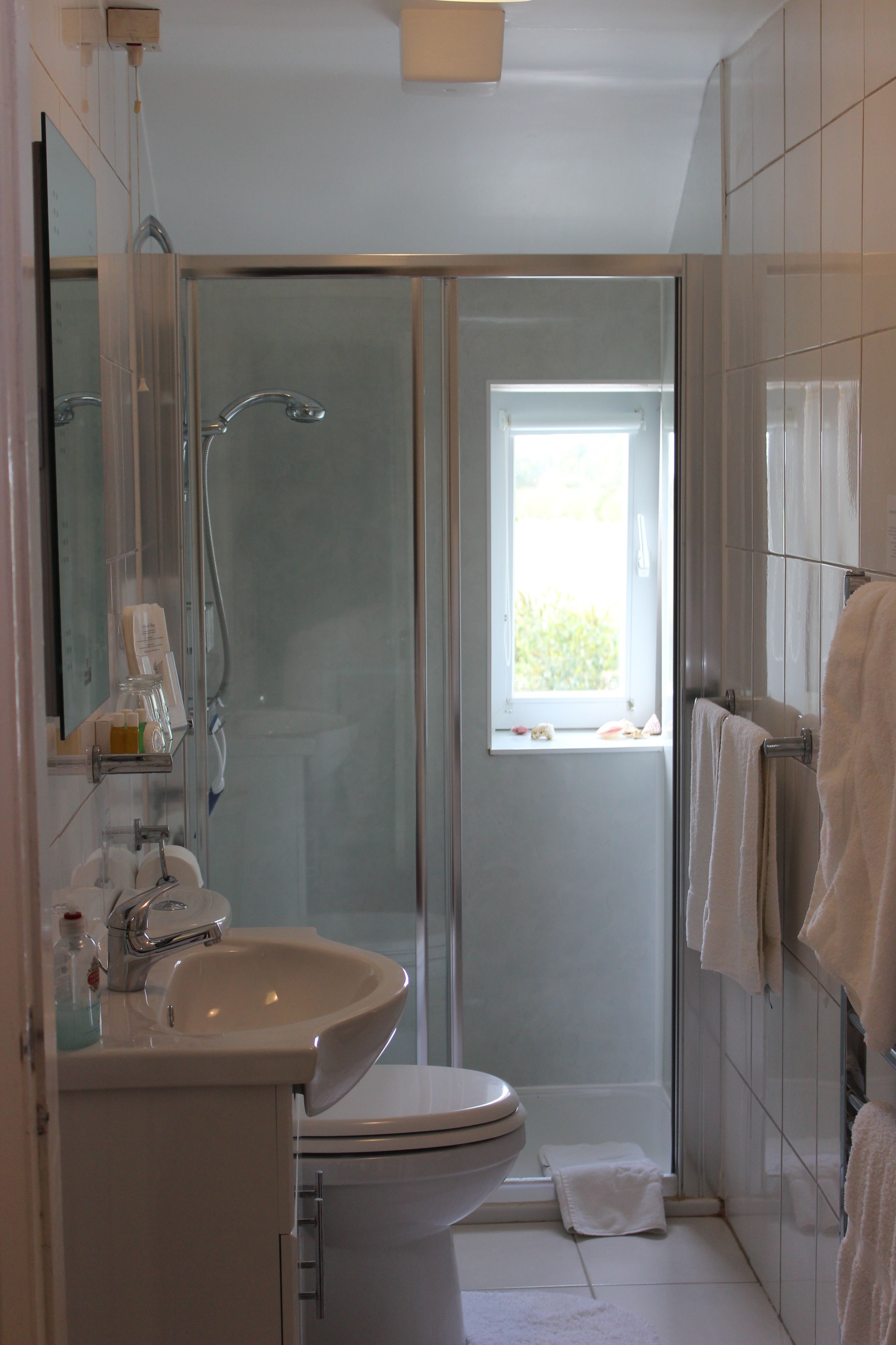 A modern bathroom with a glass shower enclosure, a toilet, a sink, and a window providing natural light.