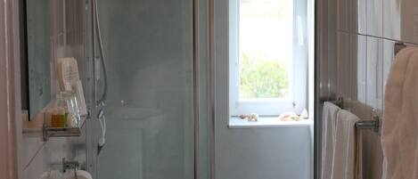 A modern bathroom with a glass shower enclosure, a toilet, a sink, and a window providing natural light.