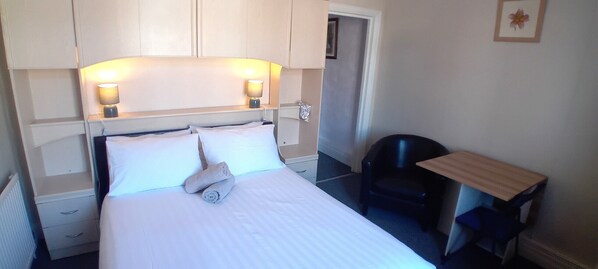 A hotel room with a bed, two bedside lamps, a chair, a small table, and a door. - Home and Away Guesthouse (Bridlington)
