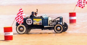 A vintage car with the number 172 driving on a sandy surface with red and white striped barriers. - Home and Away Guesthouse (Bridlington)
