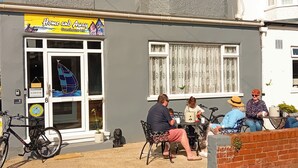 A guesthouse with a signboard, bicycles, and a group of people seated outside. - Home and Away Guesthouse  (Bridlington)