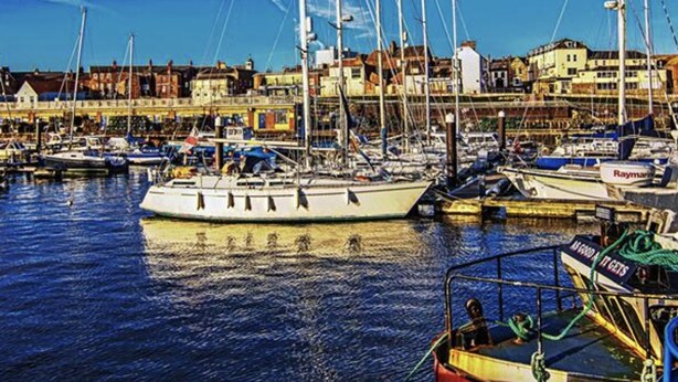A marina with several sailboats docked, a red boat in the foreground, and buildings in the background. - Home and Away Guesthouse  (Bridlington)
