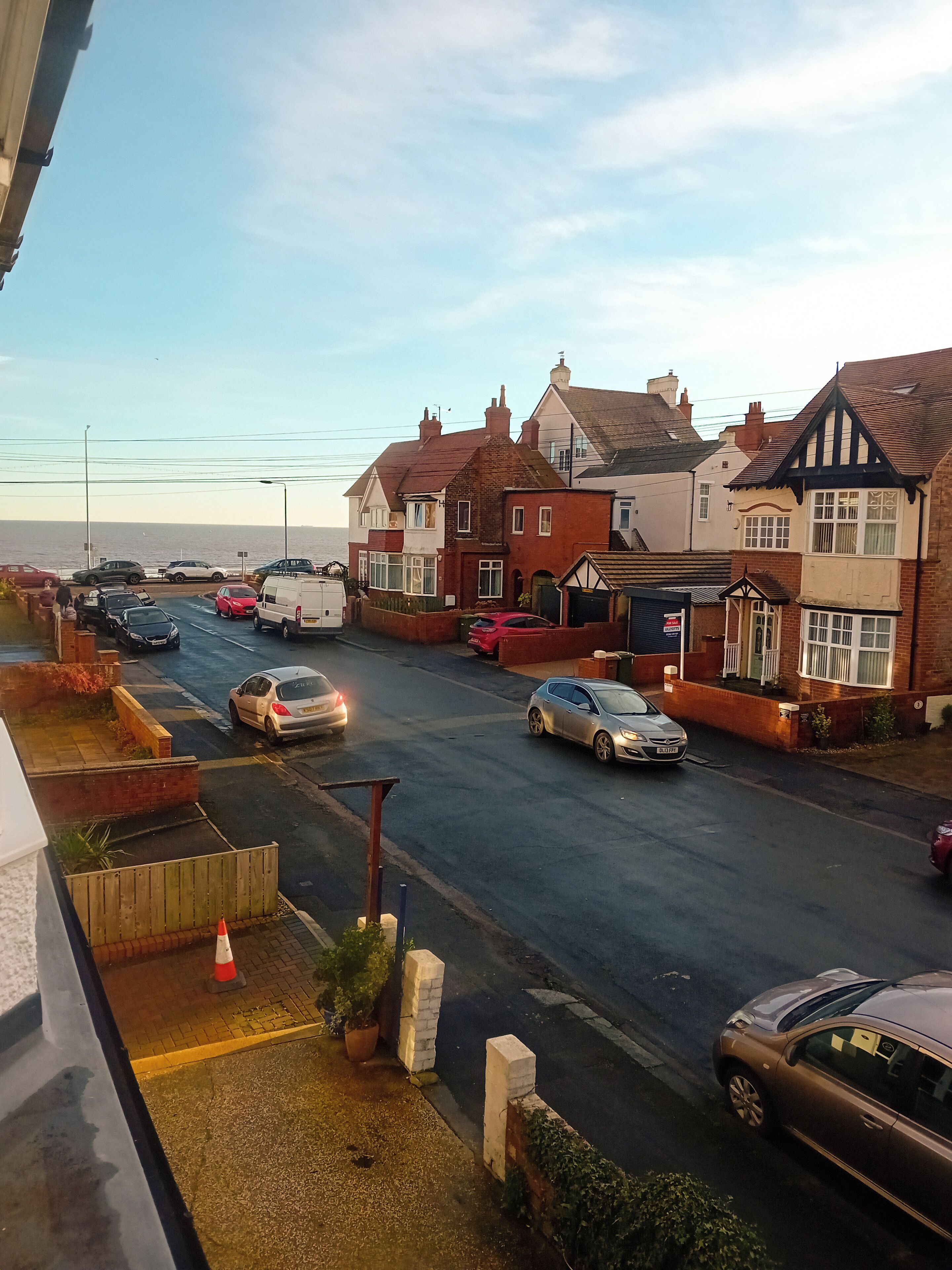 A street view with residential houses, parked cars, and a clear sky.