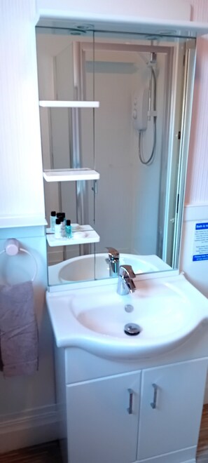 A bathroom with a white sink, a mirror, a shower, and a towel rack. - Home and Away Guesthouse (Bridlington)