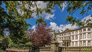 A classical building with a symmetrical facade, a central statue, and a well-maintained garden with a fence and benches. - Home and Away Guesthouse  (Bridlington)