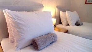 A hotel room with a neatly made bed, a rolled towel, and a nightstand with a lamp. - Home and Away Guesthouse  (Bridlington)