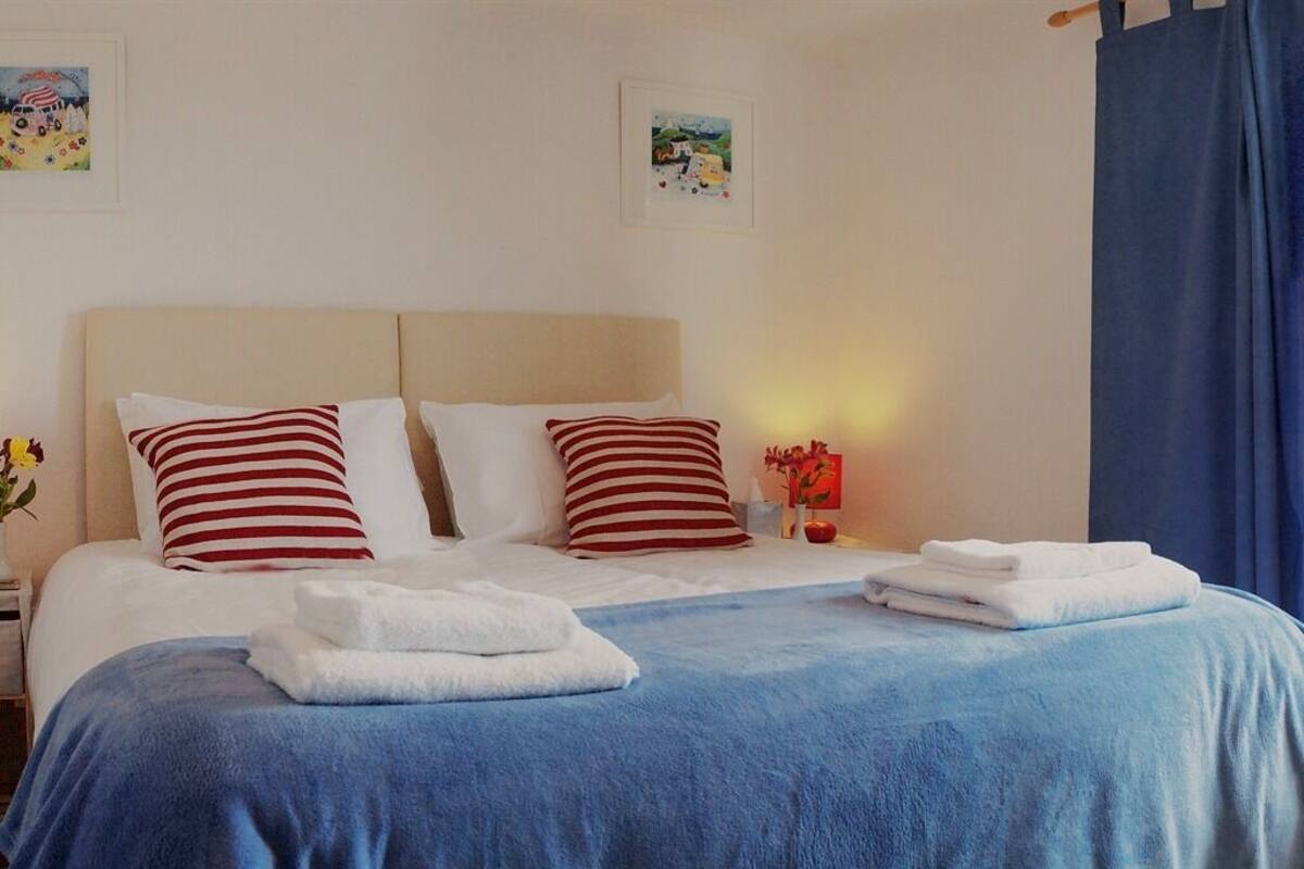 A neatly made bed with striped pillows, a blue blanket, and folded towels on a white bedspread.