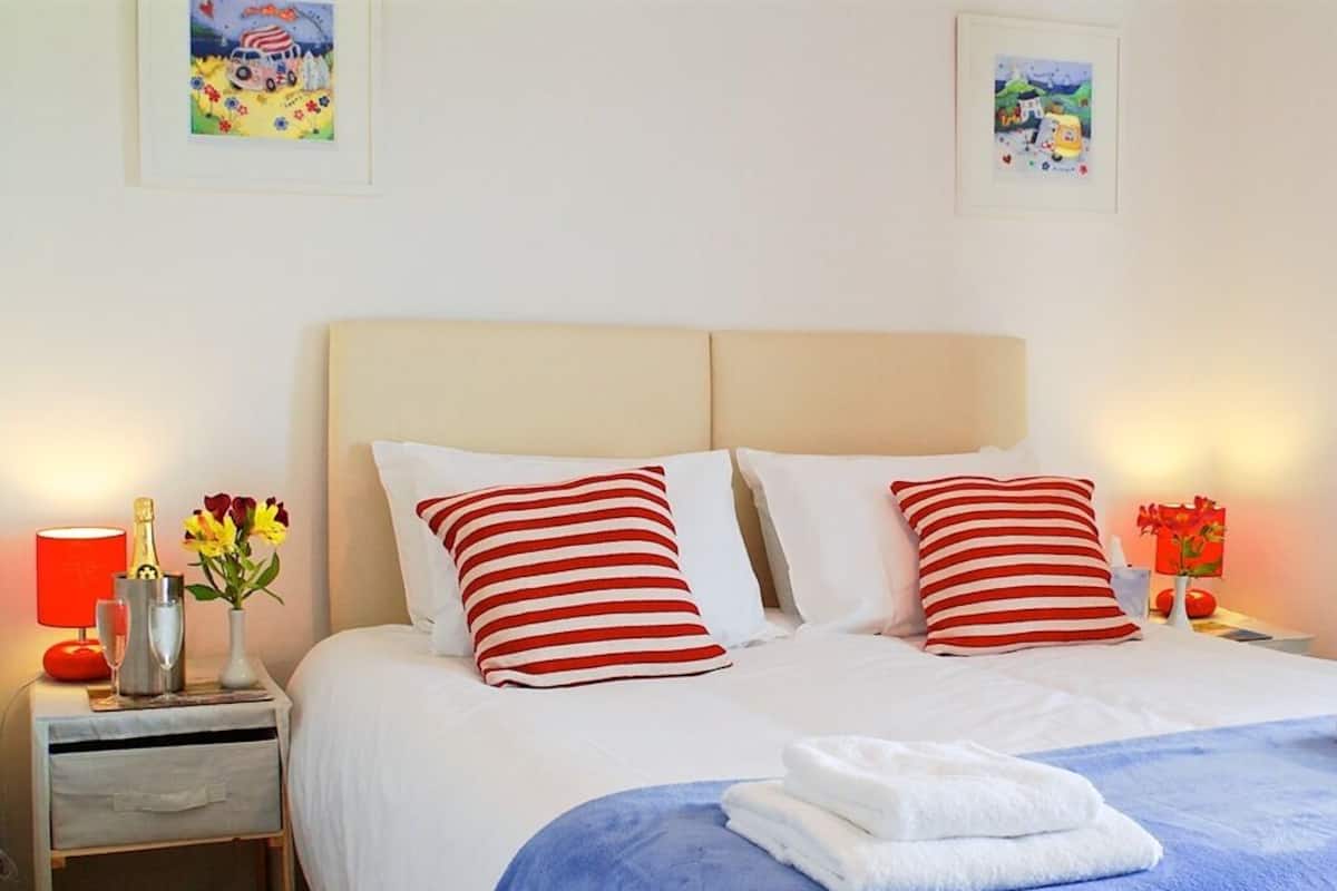 A neatly made bed with striped pillows, a blue blanket, and a folded white towel. There are two bedside tables with lamps and a vase of flowers.