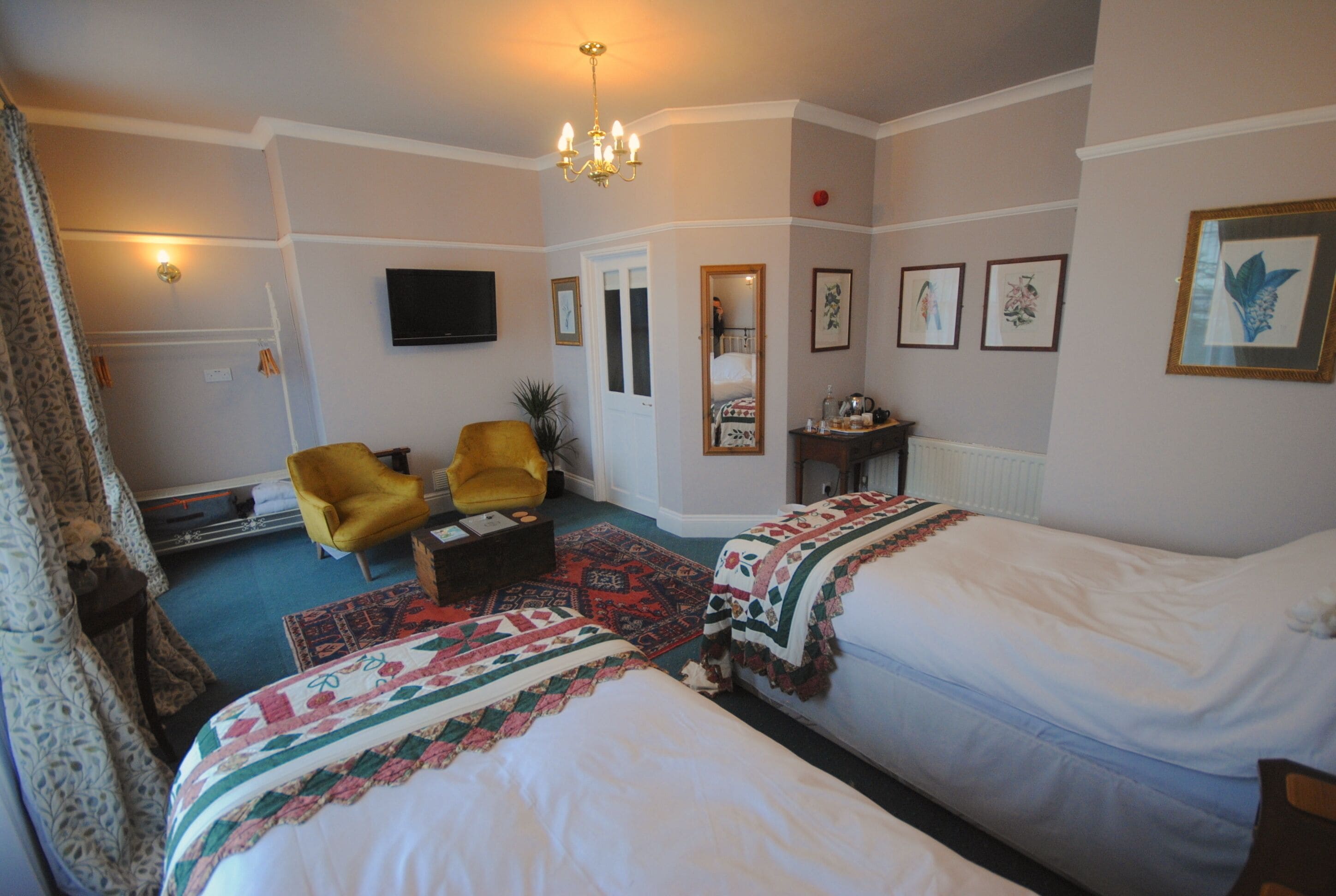 Une chambre d’hôtel avec deux lits, un fauteuil jaune, une télévision et un miroir.