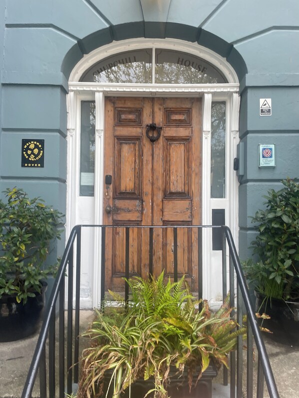 A wooden double door with a white archway, a metal handrail, and potted plants on either side. - Churchill Guest House (Dover)