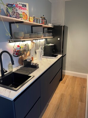 A modern kitchen with a black refrigerator, a sink, and a countertop with various items. - Churchill Guest House (Dover)