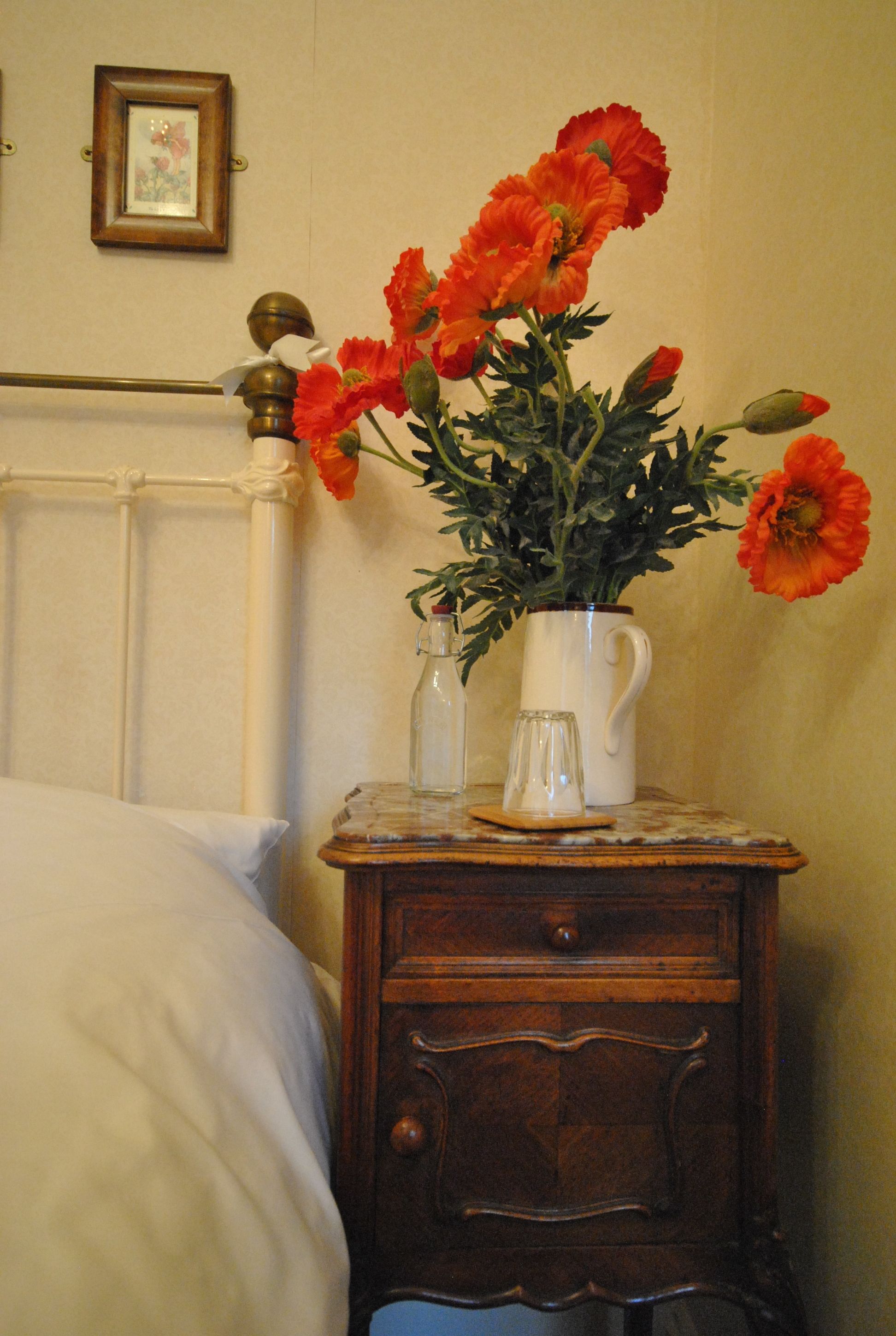 Ein Nachttisch mit einer Vase orangener Blumen, einer Glasflasche und einer weißen Tasse.