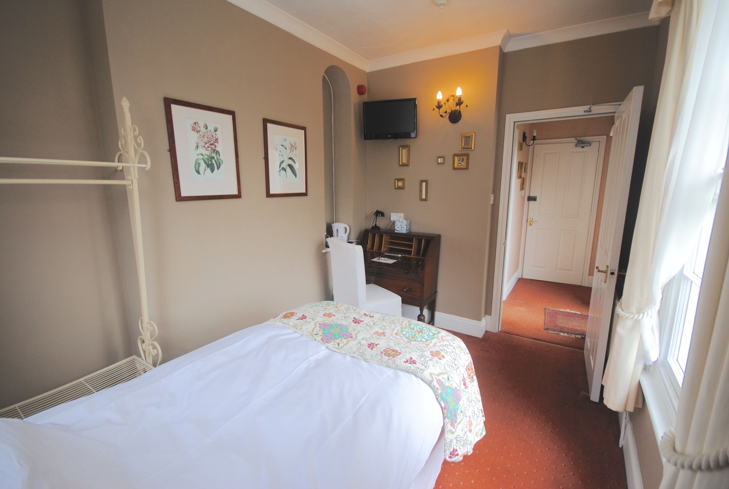 A hotel room with a bed, a desk, a chair, a television, and a door leading to another room.