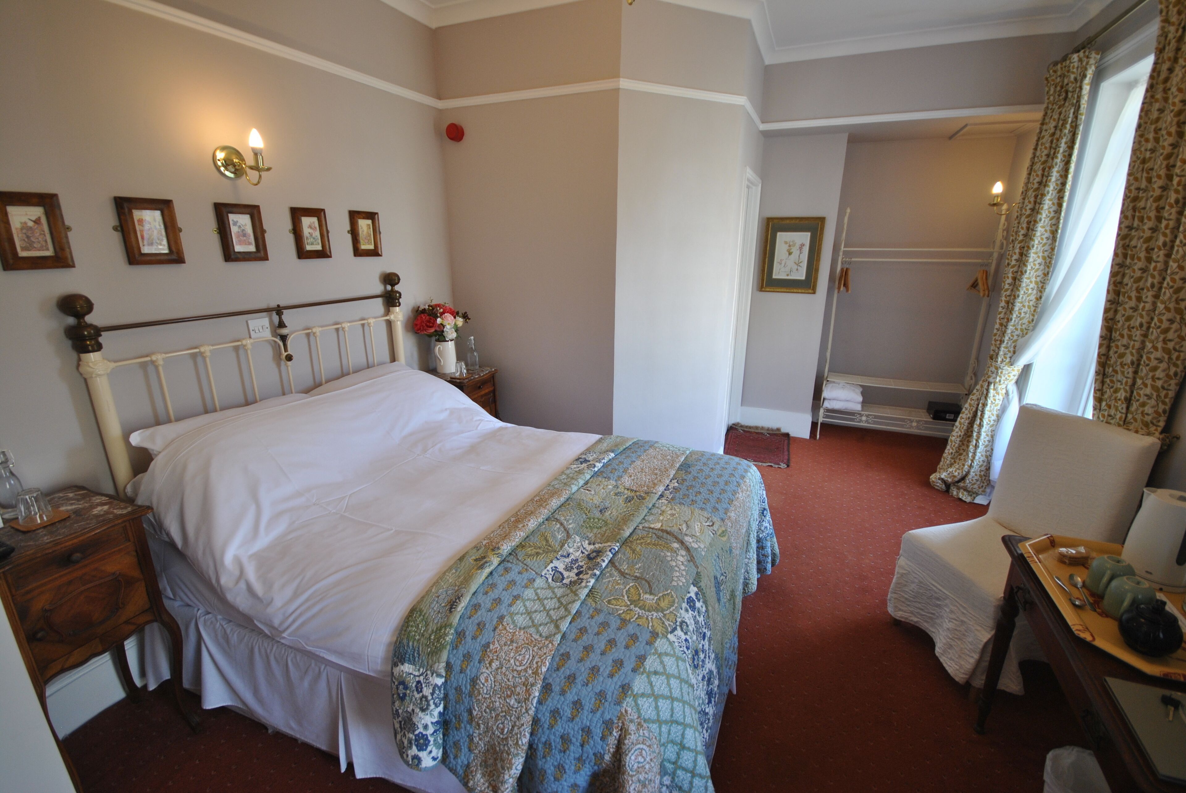 A neatly arranged bedroom with a large bed, a bedside table with a lamp, a chair, and a small table with a tray.