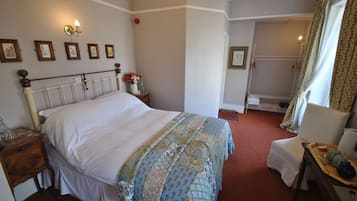 A neatly arranged bedroom with a large bed, a bedside table with a lamp, a chair, and a small table with a tray.