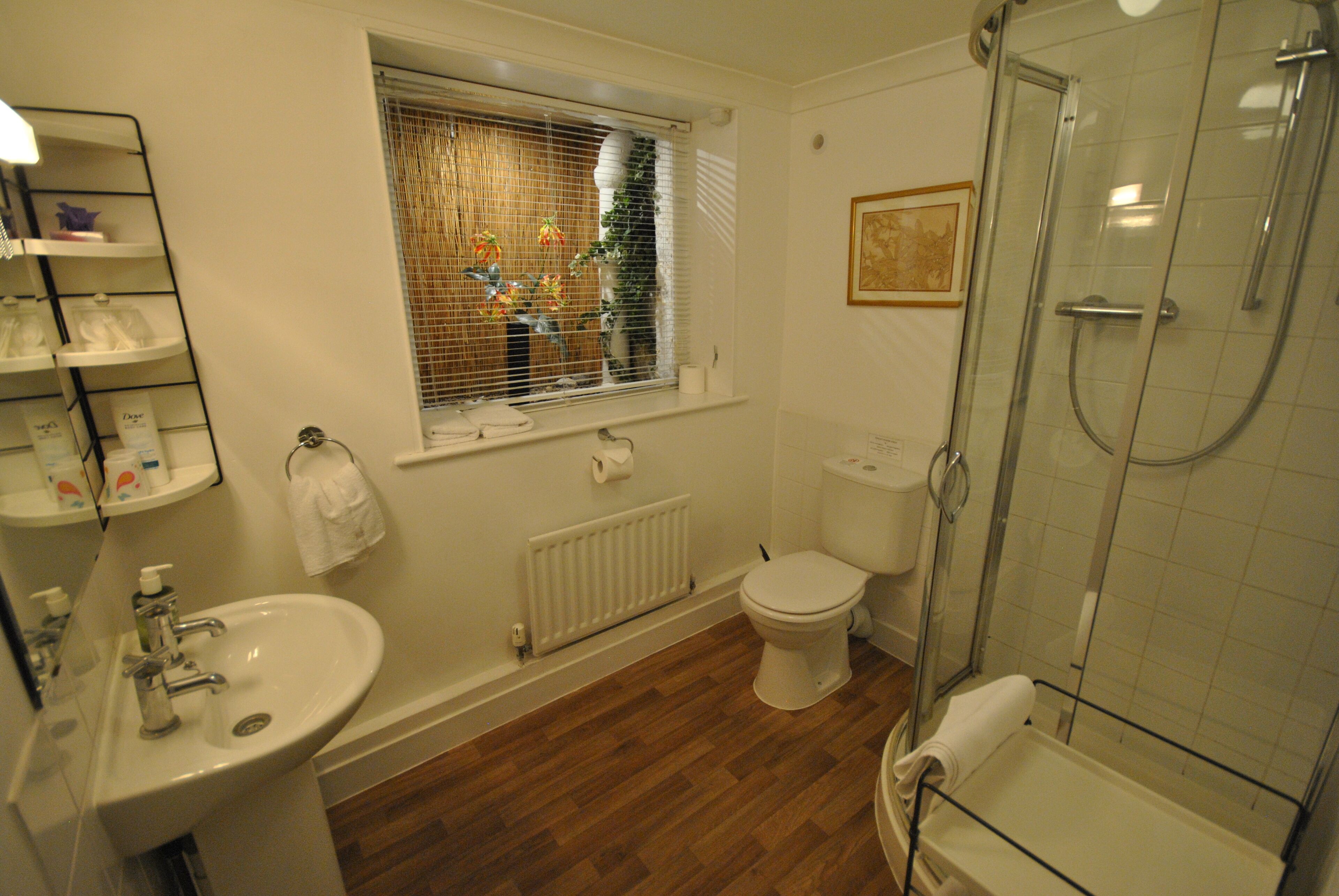 Un baño con lavabo, inodoro, ducha y ventana con persianas.