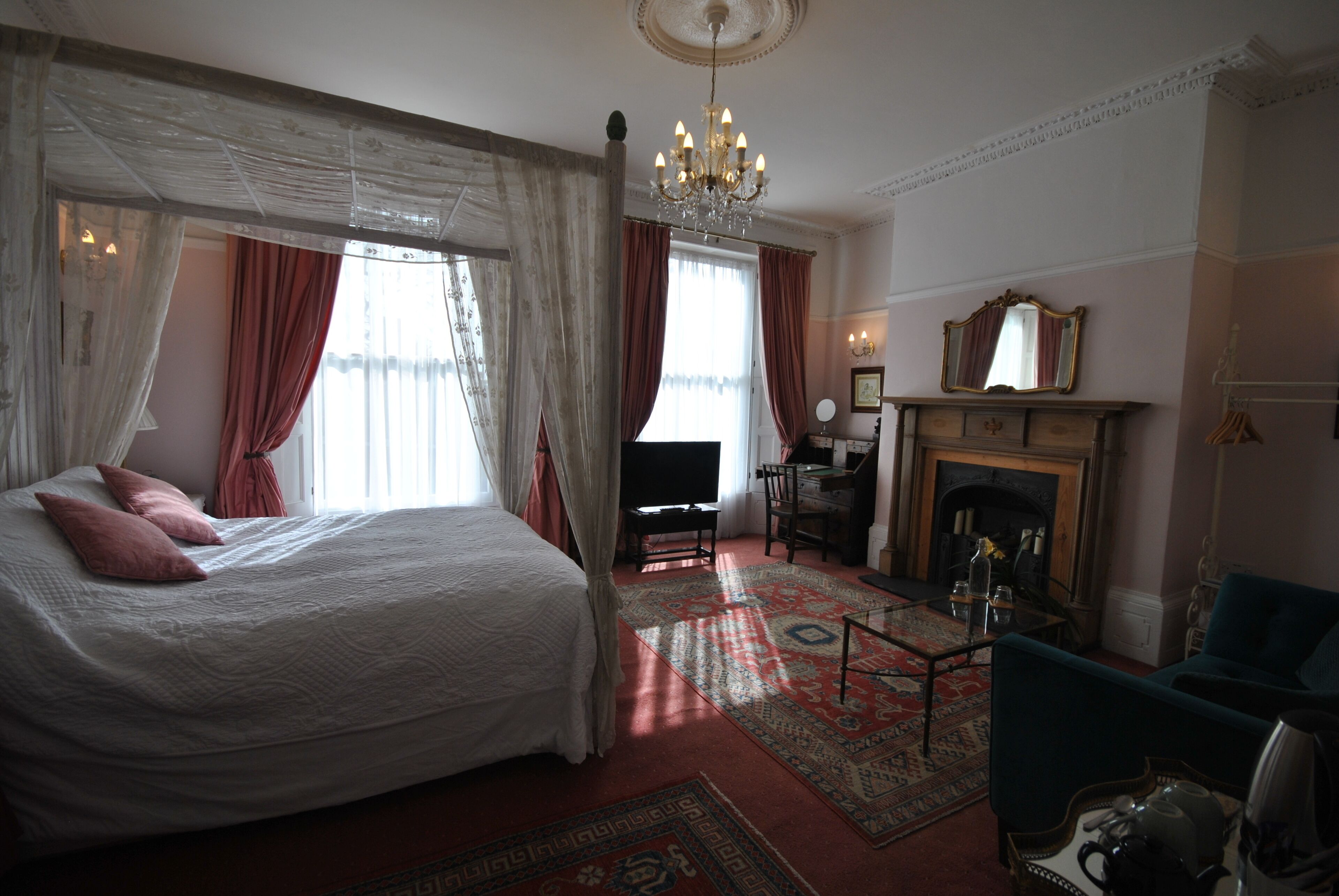 Un dormitorio con una cama grande, un escritorio, una silla, una chimenea y un candelabro.