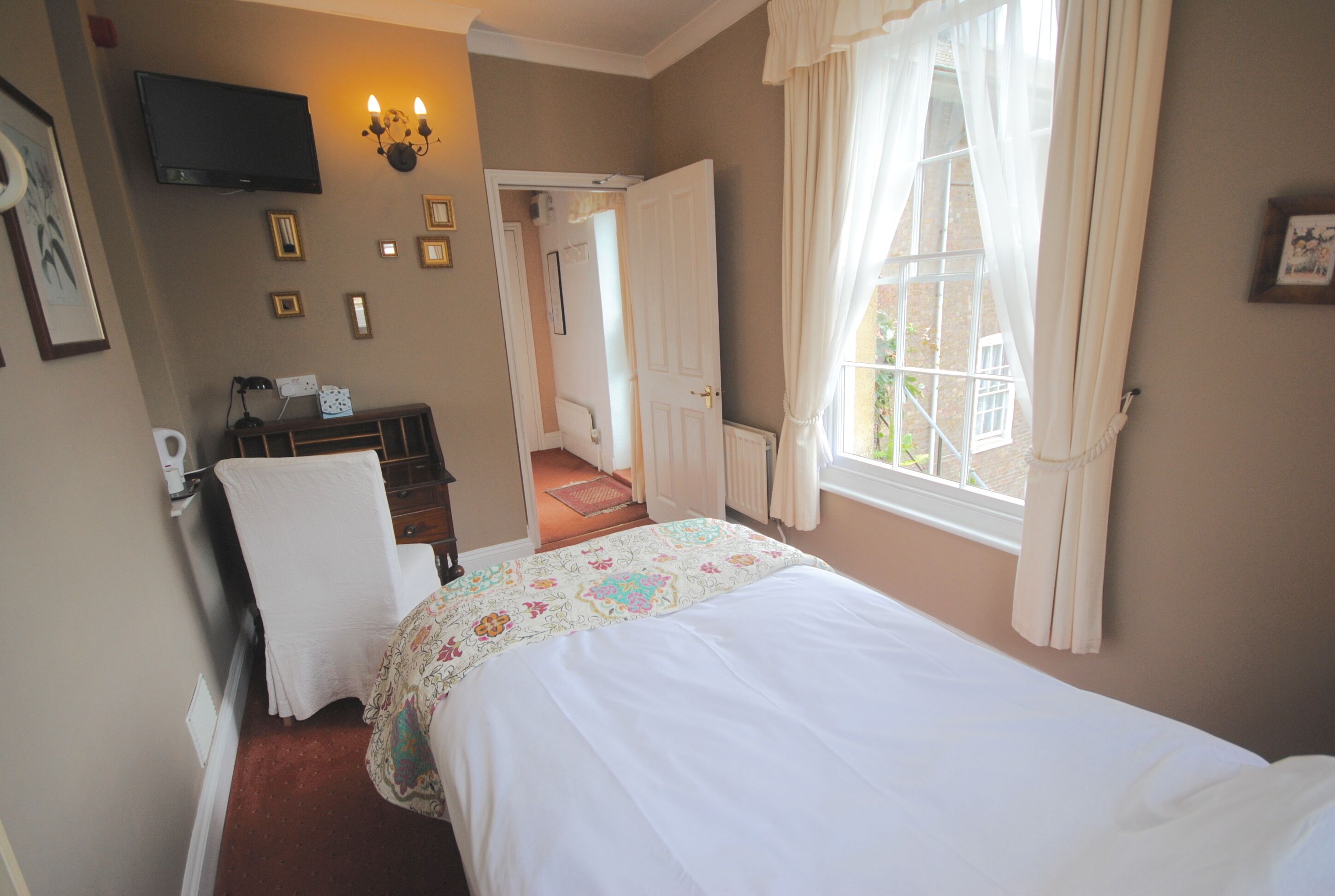 Une chambre à coucher avec un lit, un bureau, une chaise, une télévision et une fenêtre avec des rideaux.