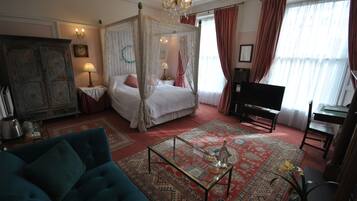 Un dormitorio con una cama con dosel, una sala de estar con sofá, una mesa de centro y un piano.