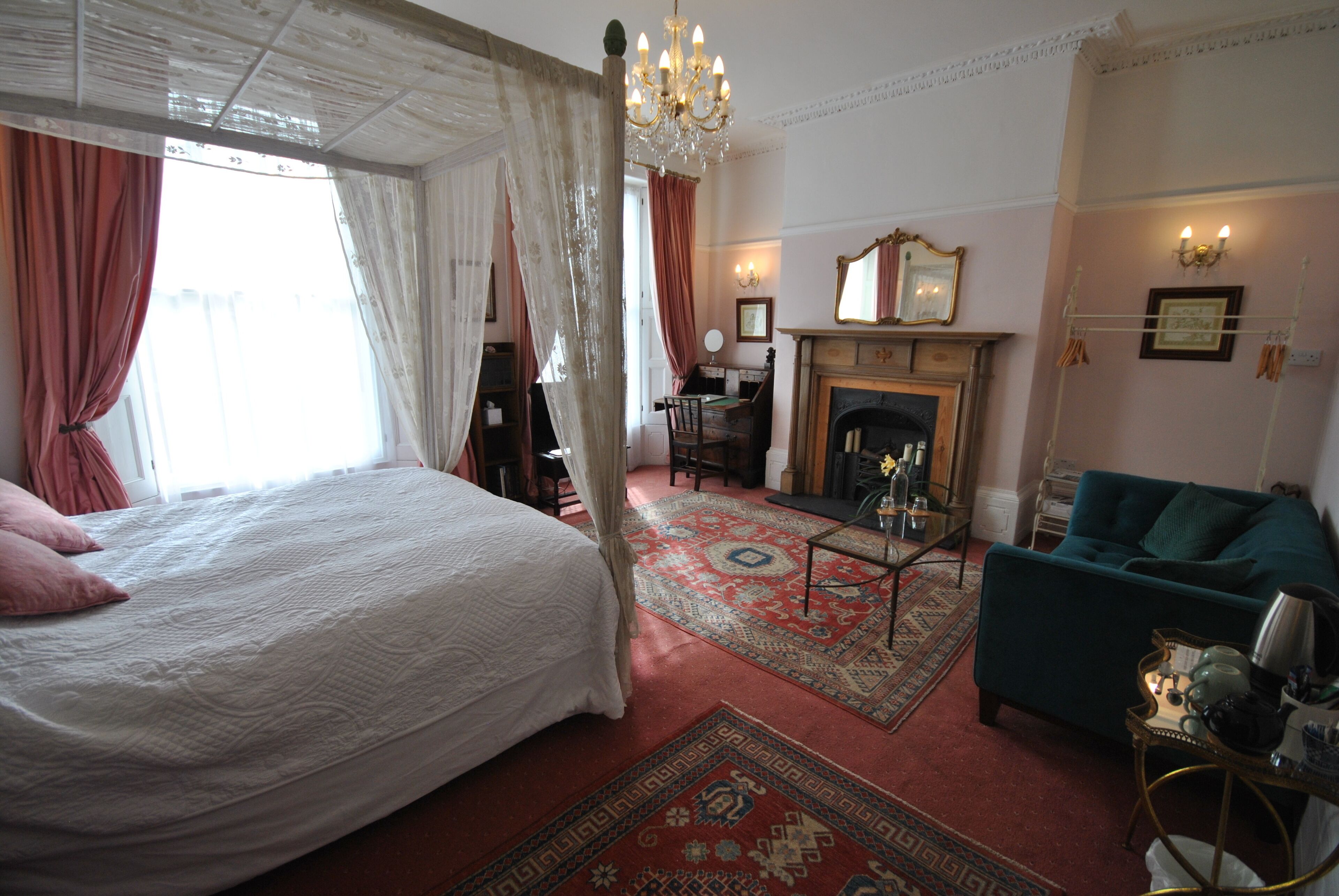 A bedroom with a large bed, a sitting area with a sofa, a fireplace, and a dining table.