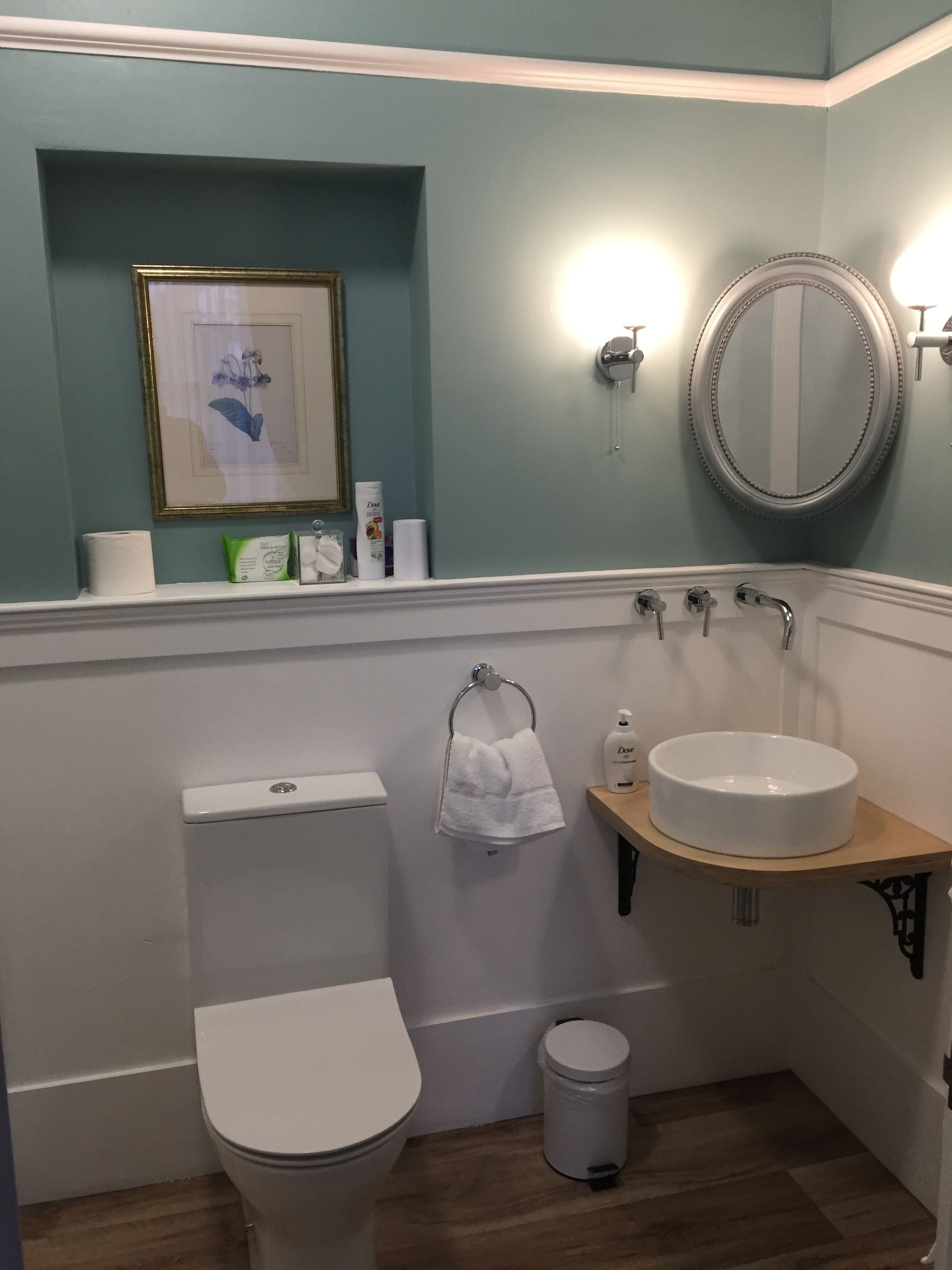 A bathroom with a toilet, sink, mirror, and a framed botanical print on the wall.
