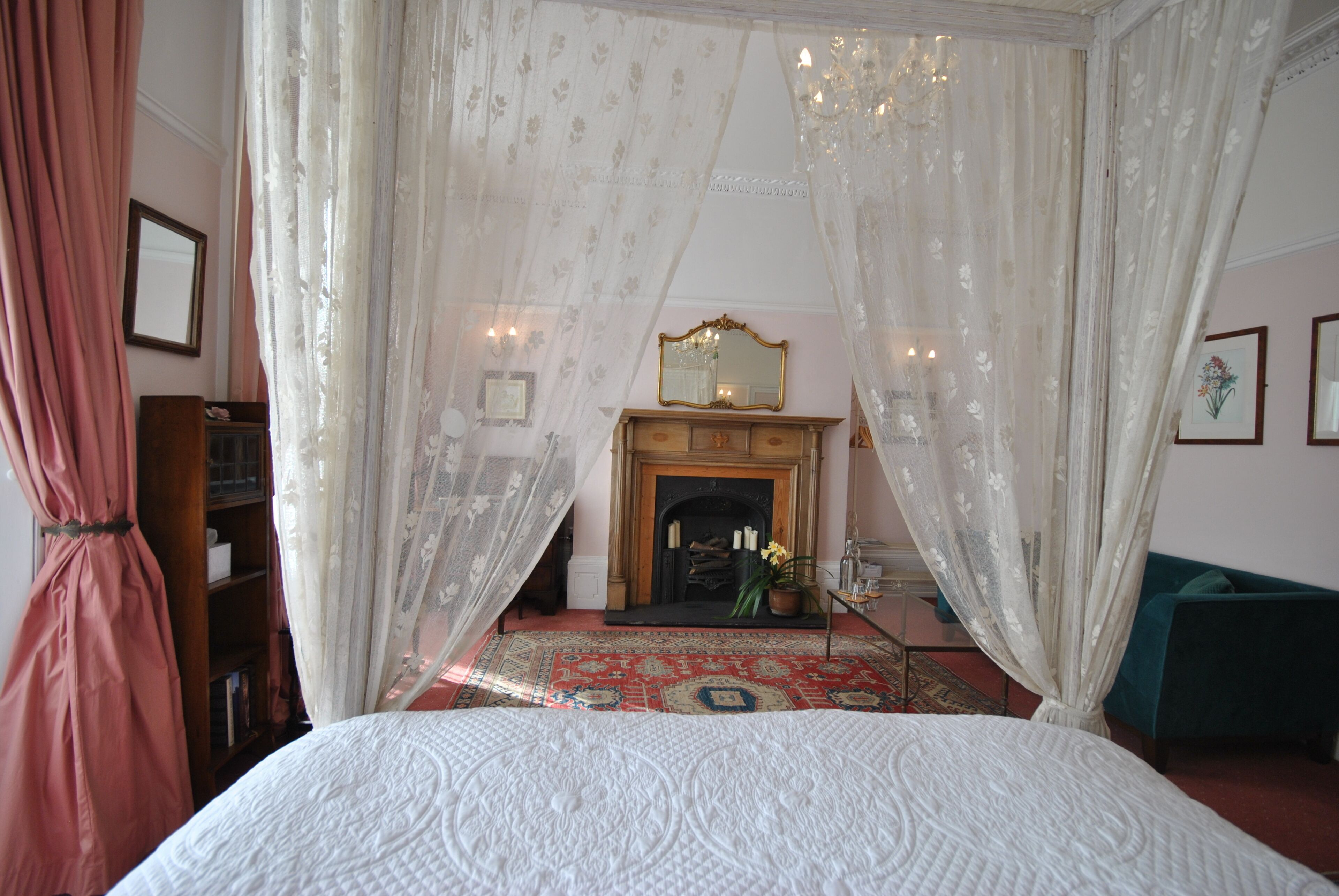 Une chambre à coucher avec un lit à baldaquin, une cheminée et un fauteuil vert.