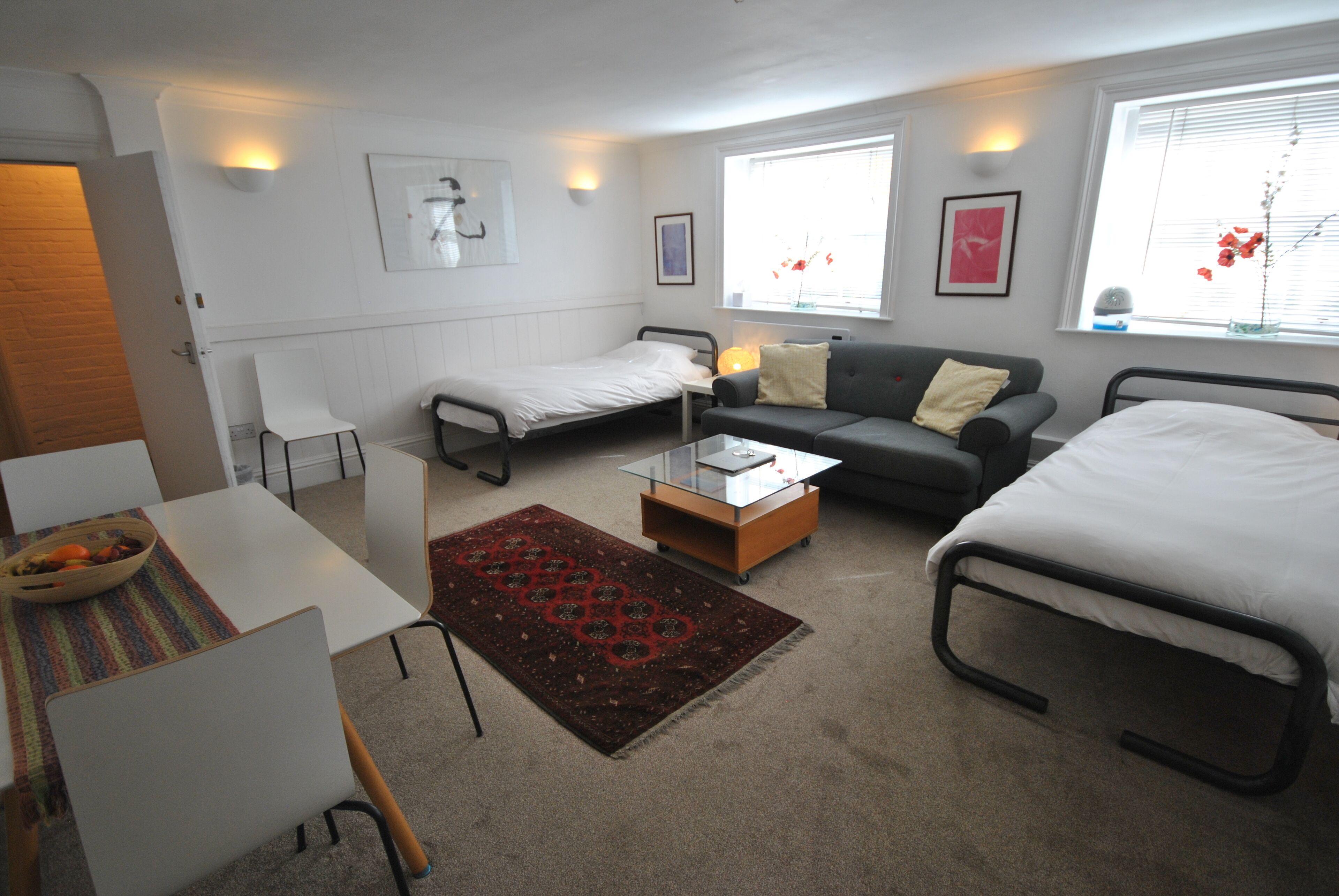 Habitación de hotel compacta con dos camas individuales, un sofá, una pequeña mesa y una silla.