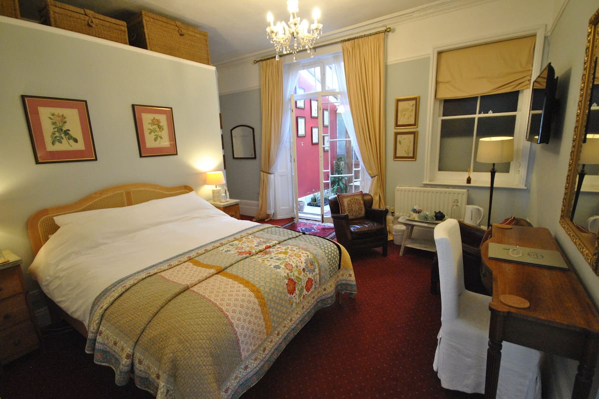 A bedroom with a large bed, a desk, a chair, a window with curtains, and a chandelier.