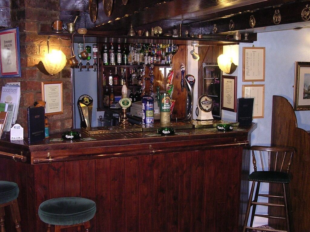 Zona de bar con mostrador de madera, taburetes y diversas botellas y vasos.