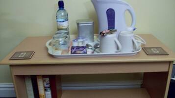 Una mesita con una botella de agua, una tetera, una taza, un pequeño recipiente y una bandeja con un teléfono y un libro.