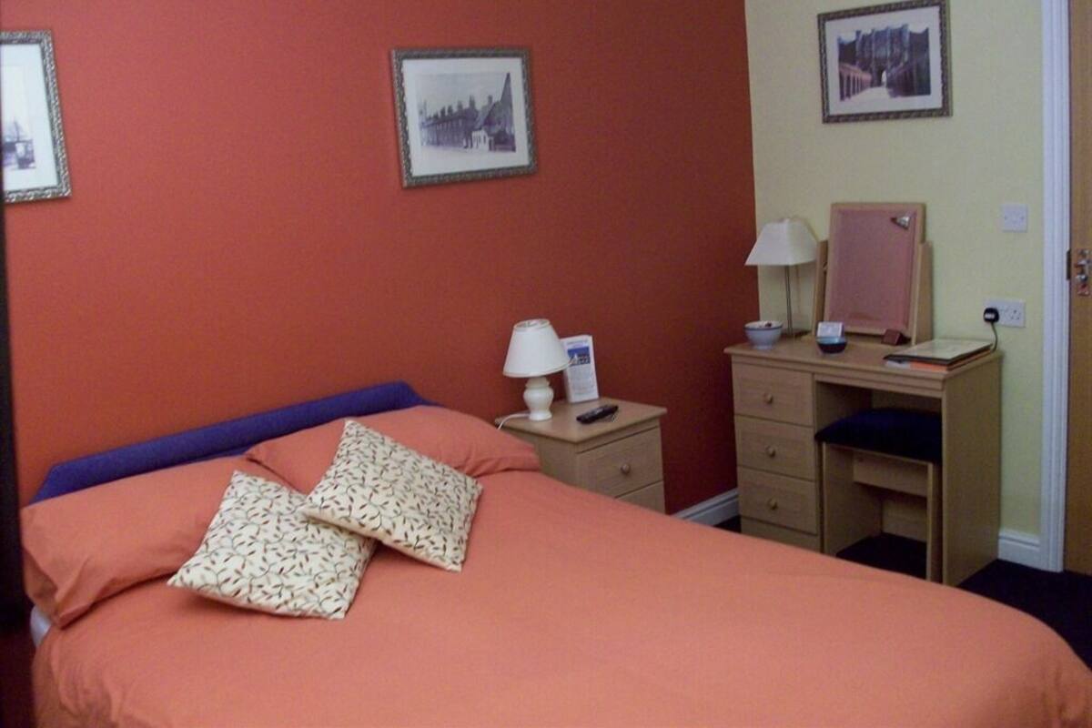 A room with a bed, a desk, and two framed pictures on the wall.