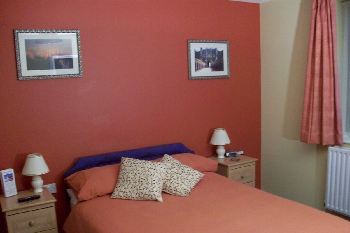 A bedroom with a bed, two bedside tables, two lamps, and two framed pictures on the wall.