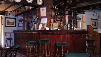A bar area with wooden stools, a bar counter, and various bottles and glasses.