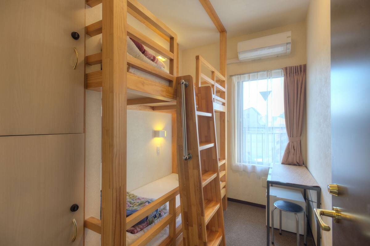 Ein kleines Zimmer mit Etagenbetten, einem kleinen Schreibtisch und einem Fenster mit Vorhängen.